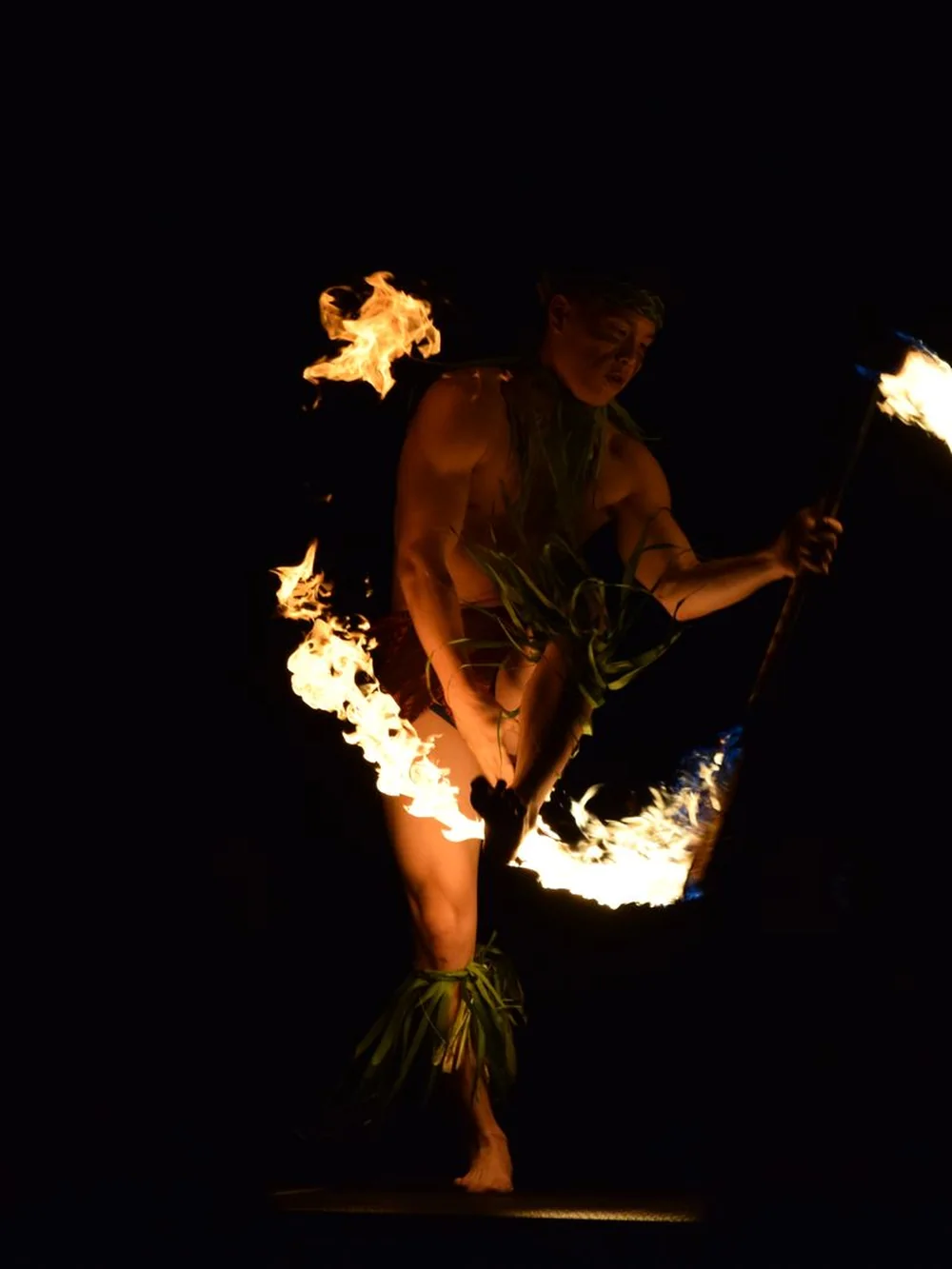 A Samoan fire-knife dancer mid-spin against a dark background, flaming blades tracing a line of light